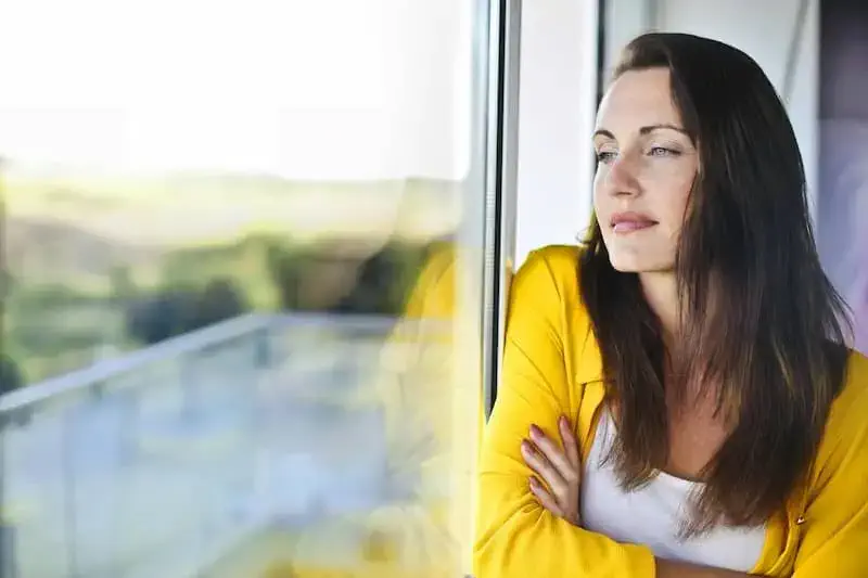 Calm woman looking out a window after breaking bad habits with clinical hypnosis at the NYC Hypnosis Center for Profound Change